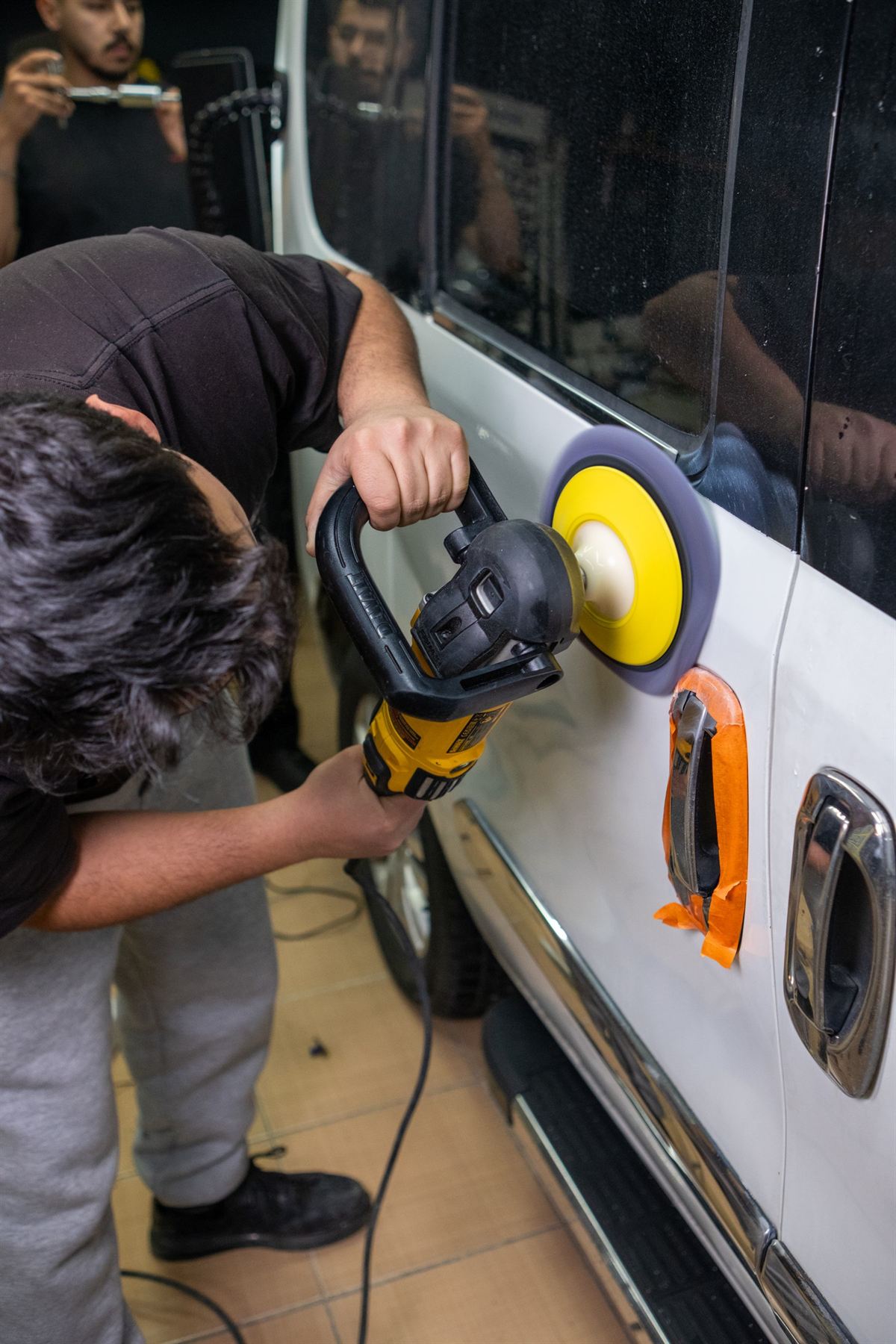 Detailer machine-polishing a car door with trim taped off